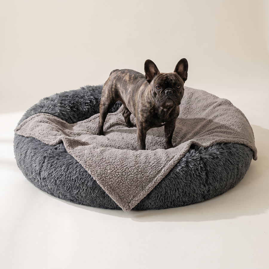 A French Bulldog resting on a donut bed lined with the Gray Pawzie Throw